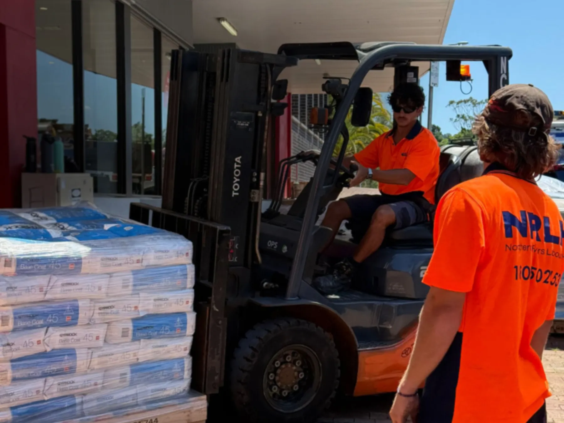 An NRLH operator on a forklift beside pallets of bagged product, a second NRLH labourer walking toward him